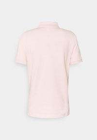 Camisa polo de manga corta color rosa claro vista desde la parte posterior, con un cuello acanalado sobre un fondo blanco liso.