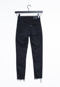 Svarta denim skinny jeans hängande på en krok, med sydda fickor, fransad nederkant och en slät yta med minimal detaljer.