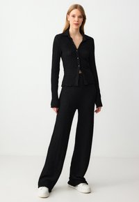 Zwart gebreid twee-delig outfit met een knoopsluiting en een kraagtop met lange mouwen en bijpassende brede broeken. Gelaagd stof met ribbelstructuur.