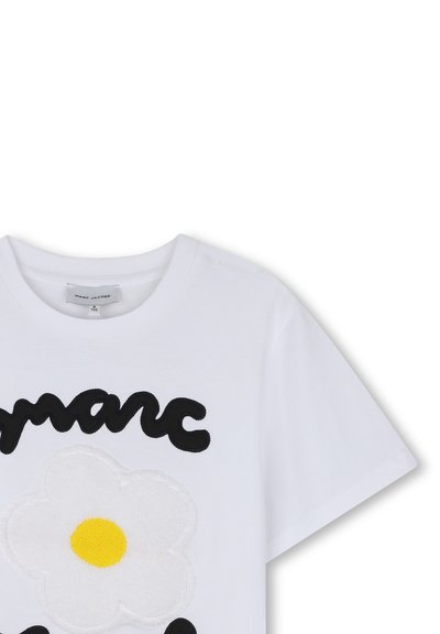Λευκό T-shirt με κοντά μανίκια, μαύρο κείμενο ""marc"" και ένα λευκό λουλούδι με κίτρινο κέντρο κεντημένο στο μπροστινό μέρος.