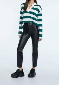 Gestreepte groen-witte longsleeve shirt, zwarte high-waisted leren broek, en zwarte chunky sneakers. Eenvoudige kraag en voorzak.