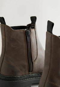 Pruunid nahast pahkluu saapad külje tõmbluku ja elastsete aktsentidega, millel on vastupidav must kummitald ja nähtavad õmblused.