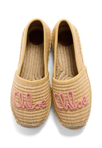 Coppia di espadrillas intrecciate beige con testo corsivo ricamato in rosa sulle punte, suola piatta e bordo color marrone chiaro intorno all'apertura.