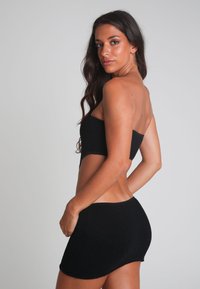 Svart stickad bandeau-topp och matchande minikjol. Tyget har ett strukturerat mönster, med en figurnära design som framhäver silhuetten.