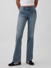 Jean en denim délavé clair avec une coupe décontractée et une jambe évasée. Comprend des poches avant et une fermeture avec bouton en métal. Porté avec des baskets noires.