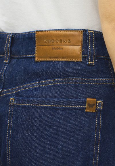 Πίσω όψη σκούρων μπλε τζιν με πορτοκαλί ραφές και καφέ δερμάτινο ταμπελάκι με την ένδειξη "WEEKEND MaxMara" στη μέση.