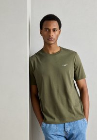 Oliven grøn bomulds-t-shirt med rund hals og korte ærmer, med et lille logo på brystet, parret med lyseblå denim shorts.