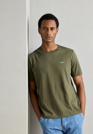 Camiseta de algodón verde oliva con cuello redondo y mangas cortas, con un pequeño logo en el pecho, combinada con pantalones cortos de mezclilla azul claro.