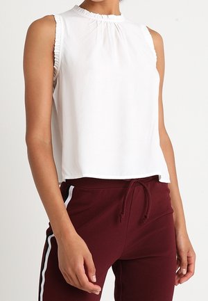 Haut blanc sans manches avec bords froncés, associé à un pantalon de survêtement bordeaux avec des bandes blanches sur les côtés et une taille à cordon.