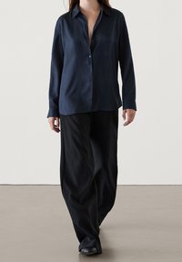 Camicia blu navy a maniche lunghe, con colletto e vestibilità rilassata, abbinata a pantaloni neri a gamba larga. Tessuto morbido e leggero.