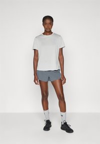 T-shirt de sport gris clair à manches courtes, associé à un short gris foncé. Des chaussures de course noires et des chaussettes grises complètent la tenue.