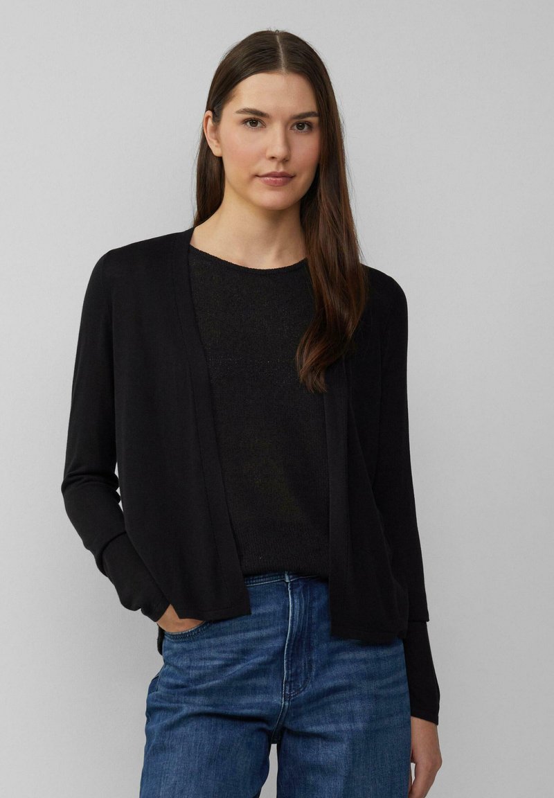 Zwarte open voorzijde cardigan van zacht materiaal, met lange mouwen en een ontspannen, iets oversized pasvorm, gecombineerd met een donkere trui.