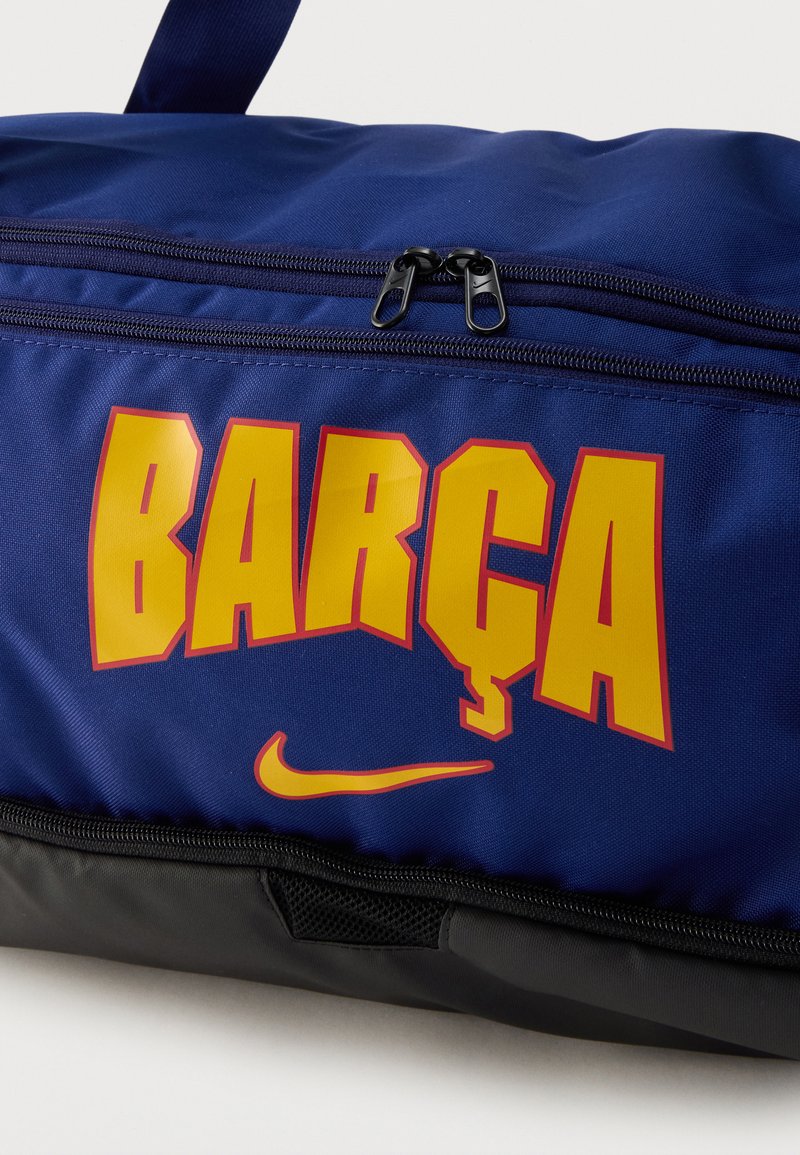 Niebiesko-czarna torba sportowa z żółtym napisem „BARÇA” i żółtym logo Nike w kształcie łuku poniżej dwóch czarnych suwaków.