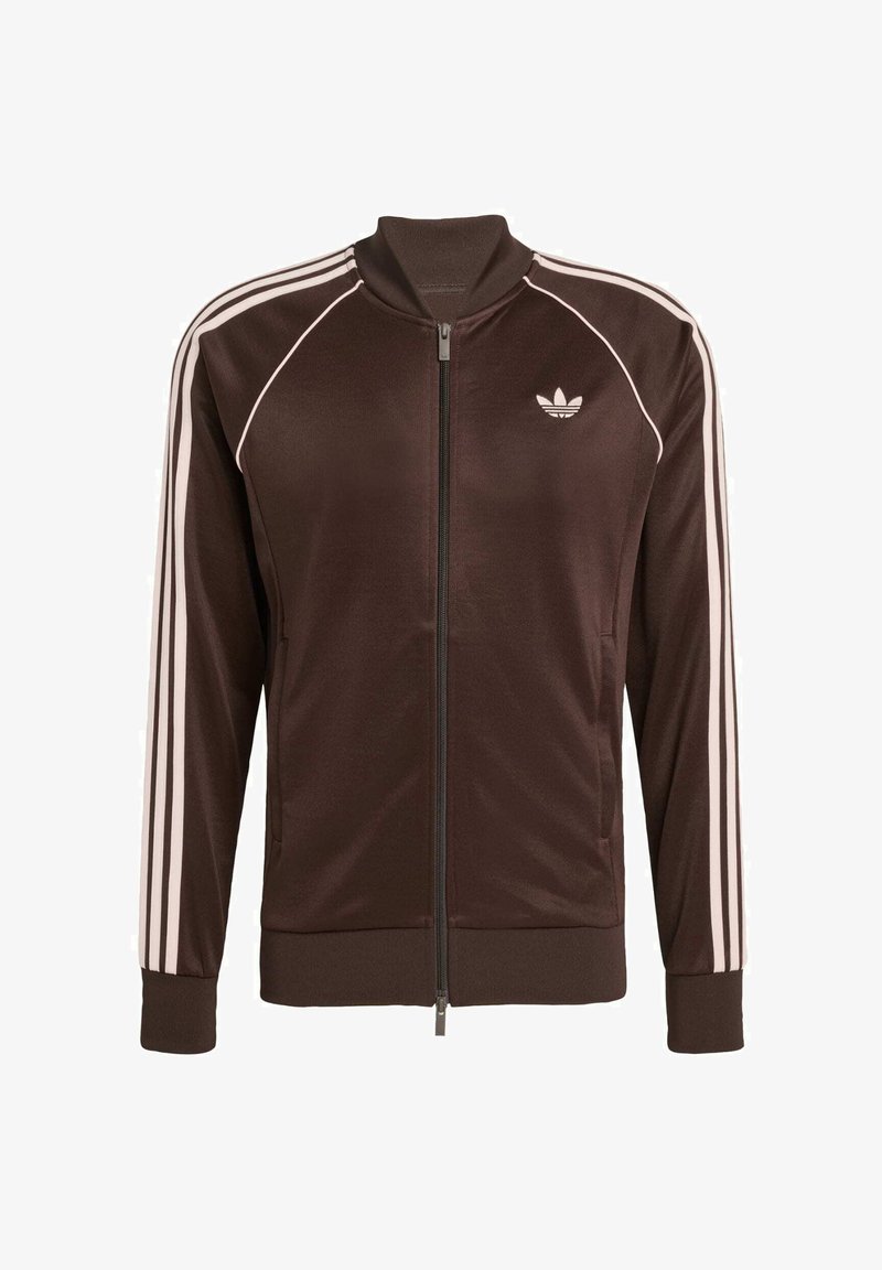 Brun zip-up jacka med vita randiga detaljer och en liten logotyp på bröstet. Tillverkad av ett glatt material med ribbade ärmslut.