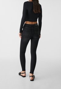 Jeans skinny negros de denim, con una cintura alta, textura suave y bolsillos traseros, combinados con sandalias planas negras.