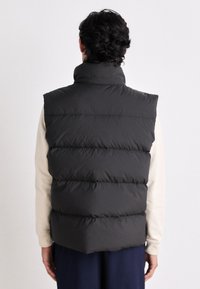Black puffer vest with high collar, quilted design, and smooth texture. Back view shows horizontal stitching and layered padding.