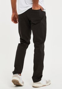 Zwarte rechte jeans met achterzakken, gecombineerd met witte sneakers met lichtgrijze en beige accenten. Glad materiaal, minimale details.