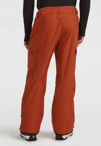 Red ski trousers with a straight cut, featuring cargo pockets and zippered ankles for ventilation. Made from water-resistant material.