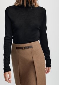 Zwarte geribbelde coltrui gecombineerd met een tan hoge taille rok met een bruine riem en gesp detail.
