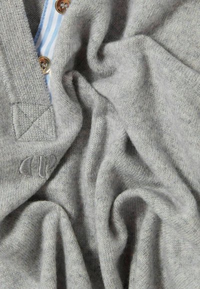 Maglione grigio a maglia con una finitura testurizzata, caratterizzato da una chiusura con bottoni e una fodera interna a righe. Il tessuto morbido si drappeggia in pieghe.