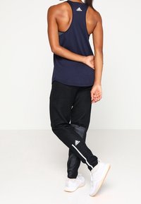 Camiseta sin mangas de color azul marino, pantalones jogger negros con acentos texturizados, rayas laterales blancas y zapatillas blancas con suelas de goma. Visibilidad de la marca Adidas.