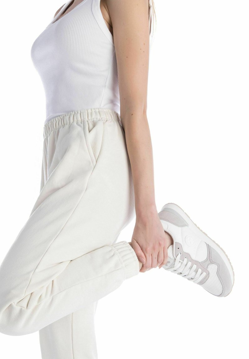 Joggers de color claro con cintura elástica, combinados con una camiseta sin mangas ajustada blanca y zapatillas de deporte con detalles grises, que muestran un ajuste relajado.