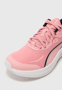 Basket de course rose avec une tige en mailles, une languette rembourrée et des lacets. Elle possède une semelle intermédiaire blanche et des accents noirs sur le talon.
