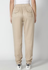 Joggers ligeros en color beige con cinturilla elástica, dos bolsillos traseros, puños ligeramente fruncidos, combinados con zapatillas plateadas.