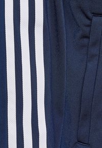 Jūras zila sporta šorti, kas izgatavoti no teksturēta auduma, ar trim vertikālām baltām svītrām un sānu kabatu.