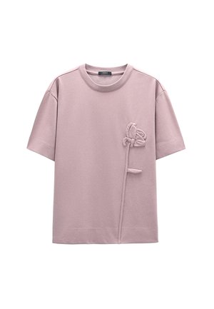 Jasnoróżowa koszulka z krótkim rękawem wykonana z miękkiego materiału. Posiada teksturowany wzór kwiatowy po lewej stronie oraz okrągły dekolt.