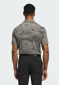 Harmaa kuviollinen polo-paita lyhyillä hihoilla, jossa on hienoinen rakenne. Yhdistetty mustiin housuihin ja vyöhön, nähtynä takaa.