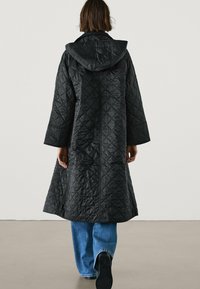 Zwart gewatteerde jas met capuchon, met een lang, losvallend ontwerp, brede mouwen en een gladde textuur, gecombineerd met blauwe wijde jeans.