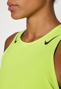 Neon grøn atletisk tank top med sorte Nike-logo accenter. Har en rund halsudskæring og et glat, letvægtsstof.