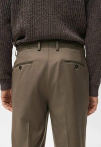 Brązowy męski sweter w prążki w zestawieniu z ciemnobeżowymi spodniami. Spodnie mają dwie tylne kieszenie z ozdobnymi guzikami i gładką fakturę.