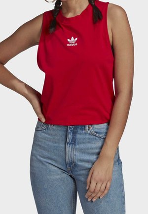 Rode sporttop zonder mouwen van katoen met een ronde halslijn en geborduurd wit Adidas-logo op de borst. Gekoeld met blauwe spijkerbroek.