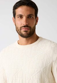 Kremowy dzianinowy sweter z fakturowanym geometrycznym wzorem, okrągłym dekoltem i prążkowanymi mankietami, wykonany z miękkiego, lekkiego materiału.