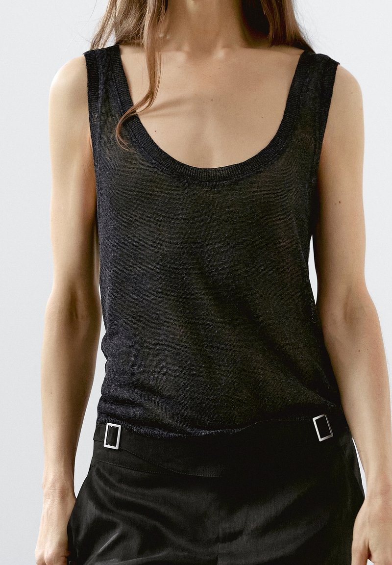 Czarny top na ramiączkach z dekoltem w kształcie litery U, wykonany z teksturowanego, lekkiego materiału. Posiada szerokie ramiączka i dopasowany krój z akcentami w postaci srebrnych elementów metalowych.