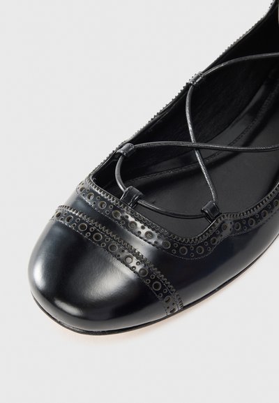 Black leather ballet flat with rounded toe, featuring decorative perforated accents and crisscross lace detailing across the upper.