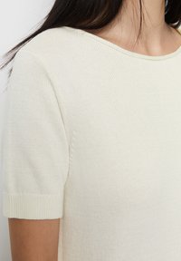 Maglione corto a maniche corte in maglia strutturata, con scollo ampio e orlo a costine, che presenta una finitura del tessuto liscia.