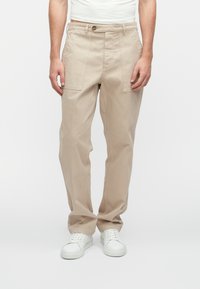 Beige auduma bikses ar brīvu piegriezumu, ar divām priekšējām kabatām, pogu aizdari un smalkām šuvju detaļām. Kopā ar baltiem sporta apaviem.