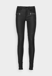 Svarta fusk läder skinny byxor med framfickor med dragkedja och knä söm detaljer på vit bakgrund.