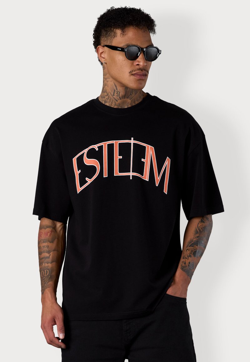 T-shirt noir oversize avec un graphique 'ESTEEM' en rouge. Fait en coton, avec des manches courtes et un col rond. Texture lisse.