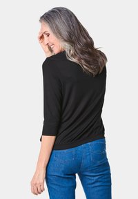 Schwarzes Dreiviertelarmoberteil mit geraffter Taille, kombiniert mit blauen Denim-Jeans mit dezenten Nähten und Gesäßtaschen.