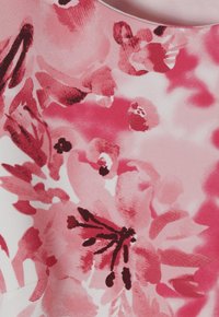 Květinová látka s velkými, abstraktními růžovými květy s tmavě červenými akcenty na bílém pozadí, jemná textura a hladký povrch.