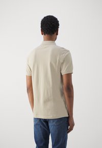 Beige polo tričko s jemnou bavlněnou texturou, krátké rukávy a klasický límec, doplněné modrými denimovými džíny. Zadní pohled.