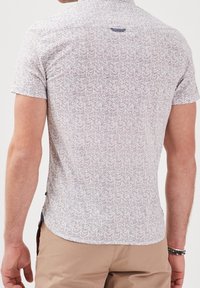 Short-sleeve button-up shirt in light fabric with a herringbone pattern in blue, red, and white tones; curved hem and collar detail.