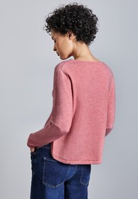 Rosa, texturerad tröja med långa ärmar, rundad nacke och avslappnad passform, tillsammans med mörkblå denimjeans.