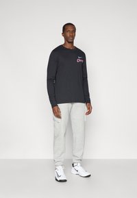 Langärmliges schwarzes T-Shirt mit "Chicago" in Rot und Blau, kombiniert mit hellgrauen Sweatpants und weißen Turnschuhen mit schwarzen Akzenten.