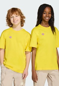 Camisetas de algodón amarillas con mangas cortas, con escote redondo y un parche de donut rosa en el lado izquierdo del pecho.