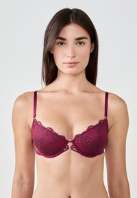Reggiseno push-up in pizzo bordeaux con bordi ondulati, dettagli decorativi nella parte frontale e spalline regolabili. Tessuto morbido con motivi intricati.